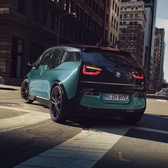 BMW i3 2018 Vista de tres cuartos de la zaga, en marcha BMW i3 I01 2018 Jucarobeige con detalles Frozen Grey metalizado, vista de tres cuartos de la zaga, en marcha en un entorno urbano