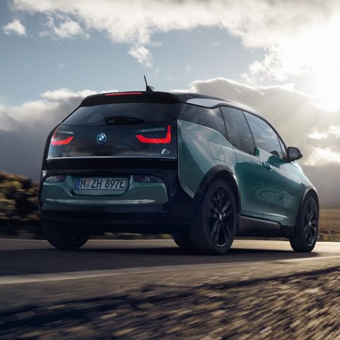 BMW i3 2018 Jucarobeige, vista de tres cuartos de la zaga, en marcha por una carretera secundaria BMW i3 I01 2018 Jucarobeige con detalles Frozen Grey metalizado, vista de tres cuartos de la zaga, en marcha por una carretera secundaria