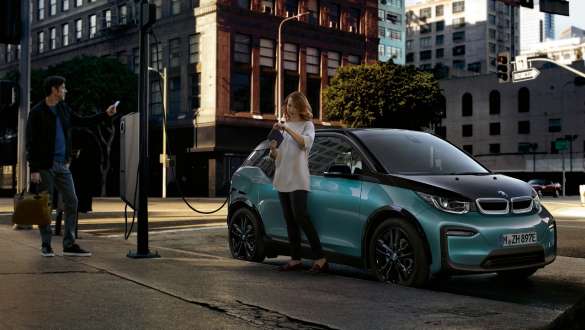 BMW i3 2018 en un punto de carga público, Jucarobeige con detalles Frozen Grey metalizado Pareja cargando su BMW i3 en un punto de carga público I01 2018 Jucarobeige con detalles Frozen Grey metalizado