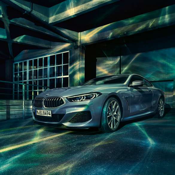 BMW M850i xDrive Coupé, vista frontal tres cuartos. BMW M850i xDrive Coupé en Barcelona Blue metálico, vistra frontal tres cuartos en alto frente a un edificio.