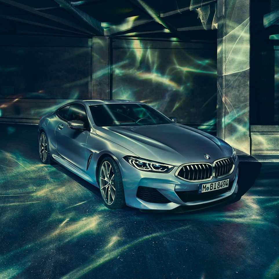 BMW M850i xDrive Coupé, vista frontal izquierda tres cuartos. BMW M850i xDrive Coupé en Barcelona Blue metálico, vista frontal izquierda tres cuartos, parado frente a un edificio.