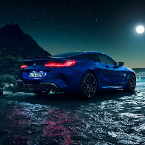 BMW M8 Competition Coupé, vista trasera tres cuartos. BMW M8 Competition Coupé en Marina Bay Blue metálico con las luces LED traseras iluminadas, vista tres cuartos en alto con luna llena.
