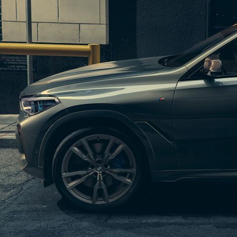 BMW X6 M50i en perspectiva lateral Hombre apoyado en un BMW X6 M50i en perspectiva lateral frente a un escenario urbano
