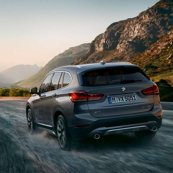 BMW X1, vista trasera tres cuartos. BMW X1, vista trasera tres cuartos frente a un escenario todo terreno.