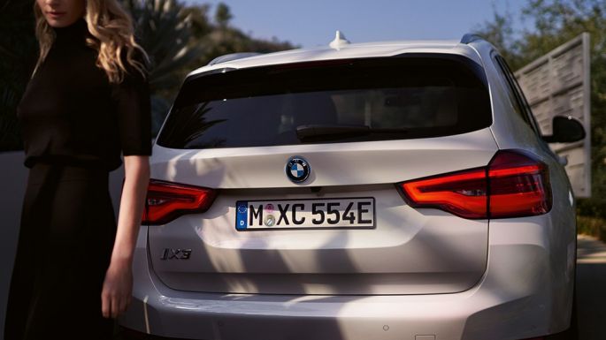 Zaga con difusor específico de BMW i BMW iX3 G08 Vista de zaga con mujer Zaga con difusor específico de BMW i BMW iX3 G08 2020 Mineralweiss metalizado Vista de zaga con mujer