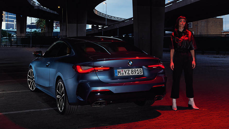 BMW Serie 4 Coupé (G22), Artic Race Blue metallic, vista de zaga con persona BMW Serie 4 Coupé (G22), Artic Race Blue metallic, vista de zaga con persona