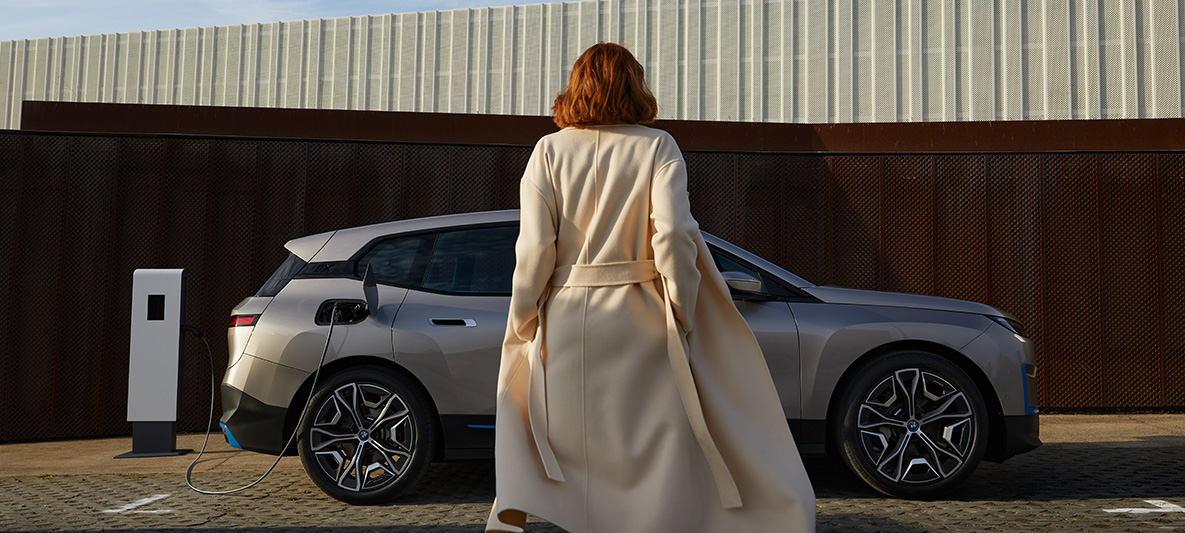 BMW iX vista lateral detenido BMW iX Cashmere Silver i20 vista lateral detenido con modelo en frente