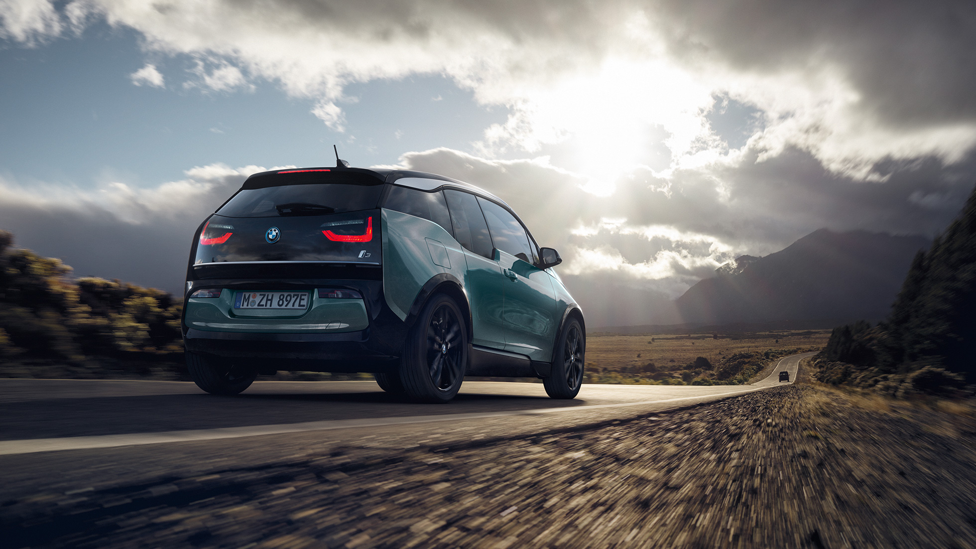 BMW i3 2018 Jucarobeige, vista de tres cuartos de la zaga, en marcha por una carretera secundaria BMW i3 I01 2018 Jucarobeige con detalles Frozen Grey metalizado, vista de tres cuartos de la zaga, en marcha por una carretera secundaria