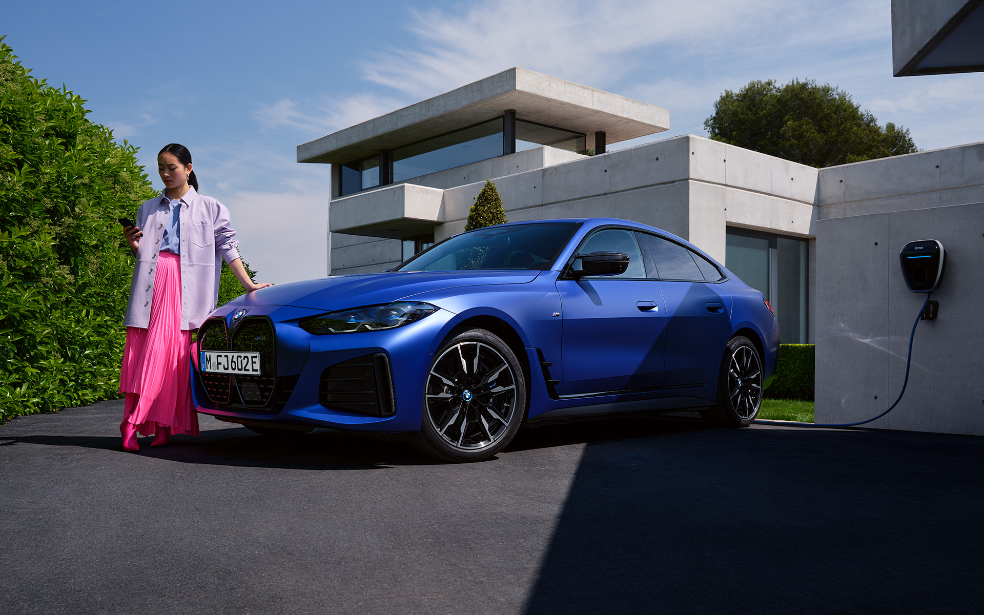 BMW i4 M50 G26 2021 BMW Individual Frozen Portimao Blau metalizado Vista de tres cuartos del frontal, parado con mujer delante de una casa