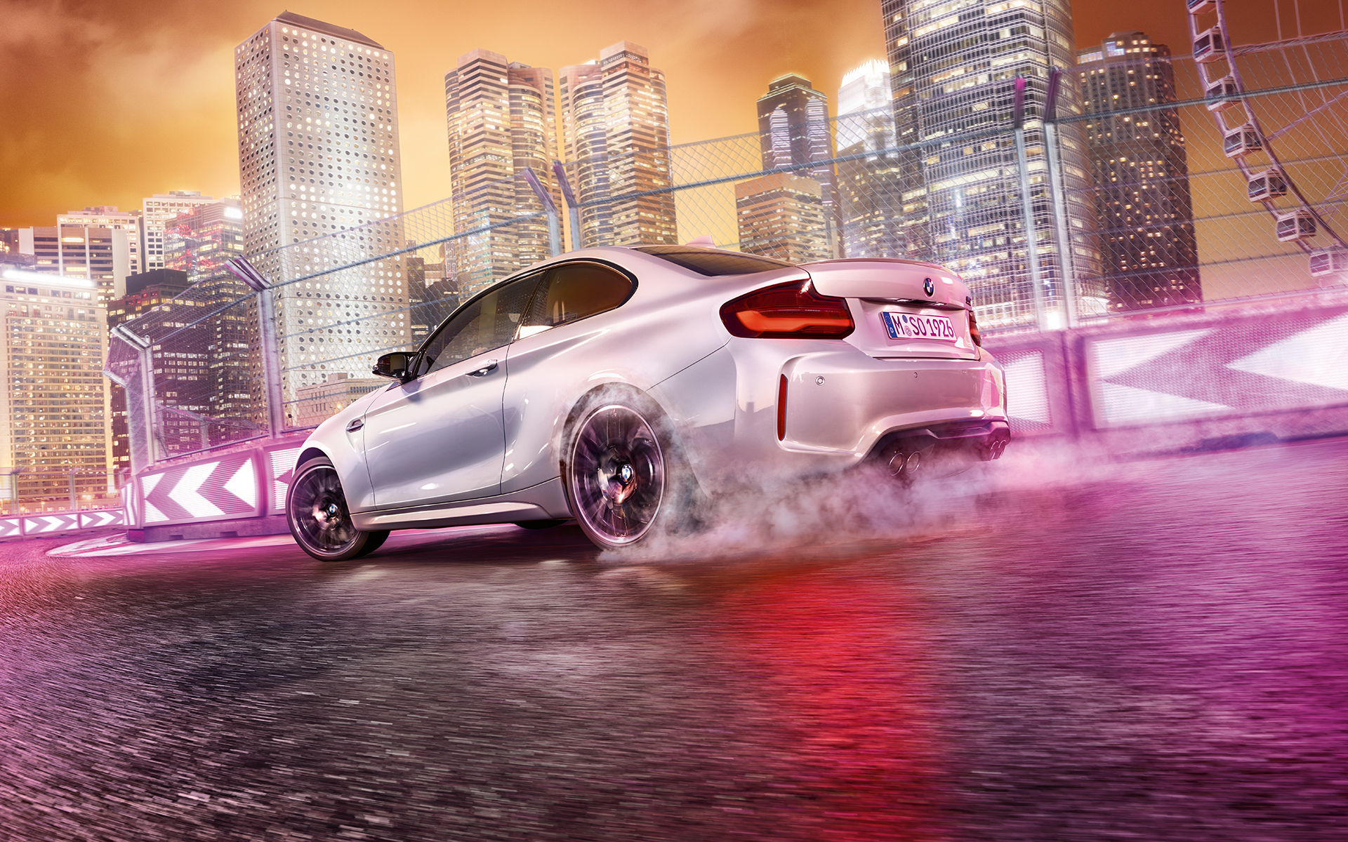 BMW M2 Competition accelera BMW M2 Competition blanco en la pista de carrera frente al paisaje nocturno de la ciudad.