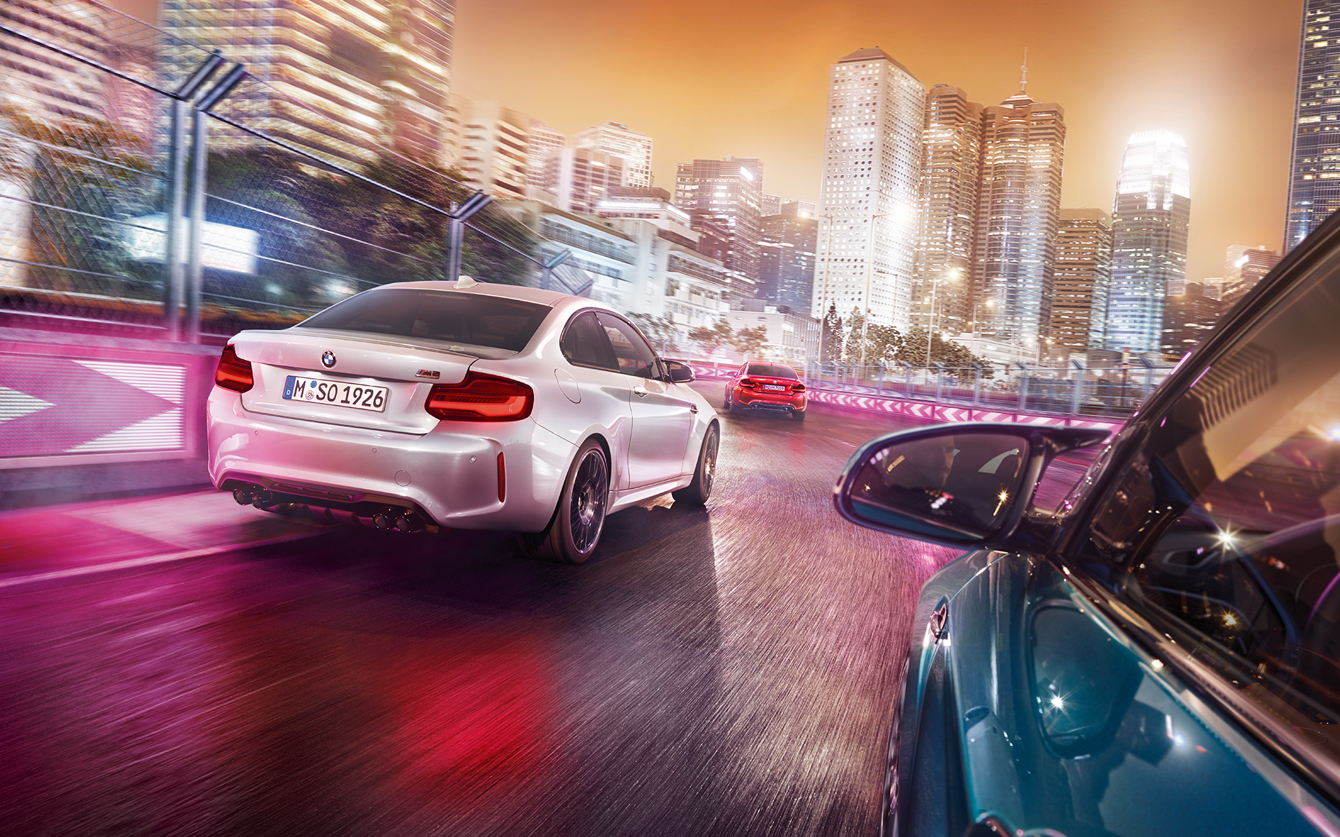 Vista posterior de un BMW M2 Competition. Vista posterior de tres BMW M2 competition en la pista de carreras con un paisaje iluminado.