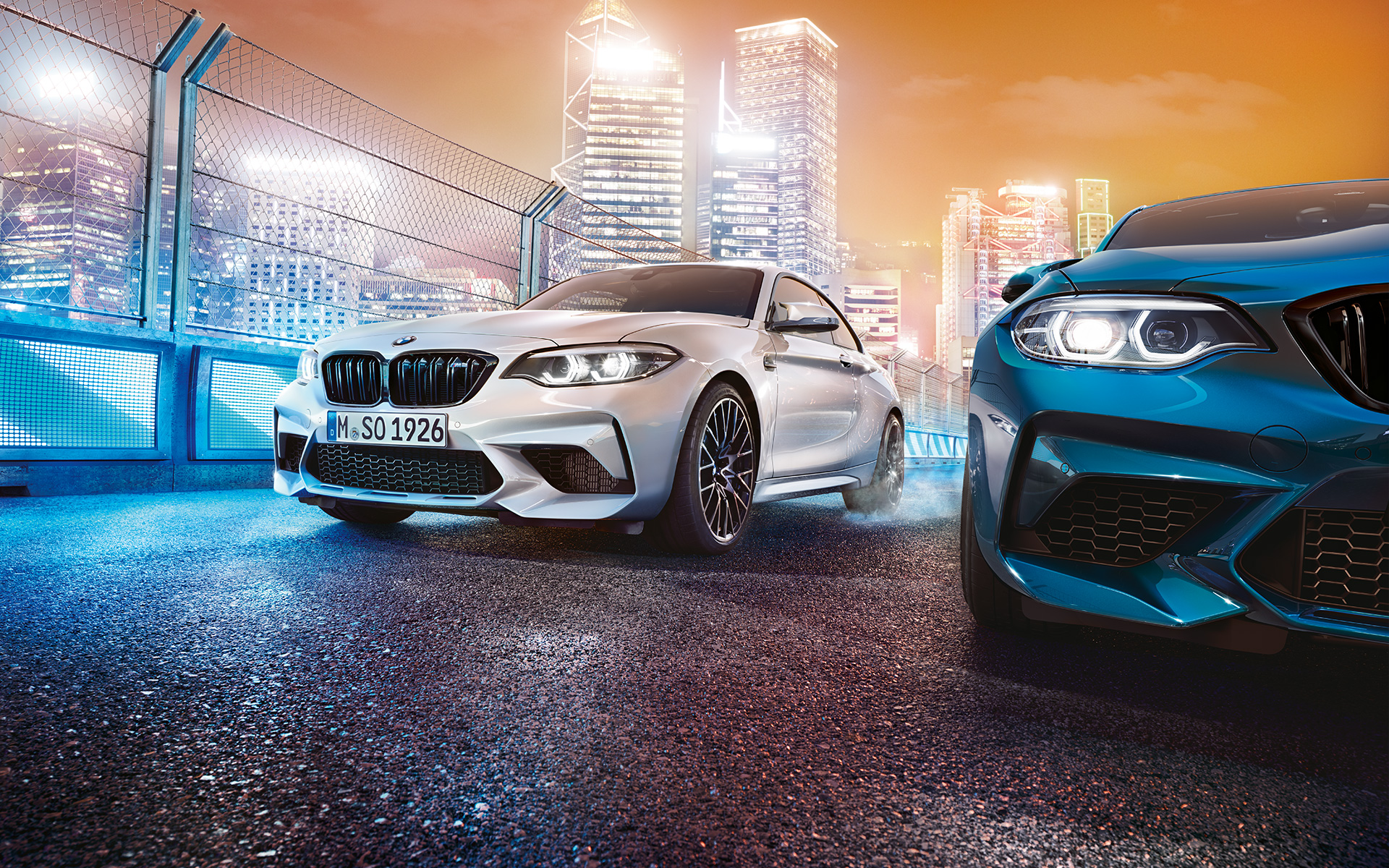 Tres BMW M2 Competition de frente. Vista trasera de tres BMW M2 Competition en la pista de carreras frente a un paisaje iluminado.