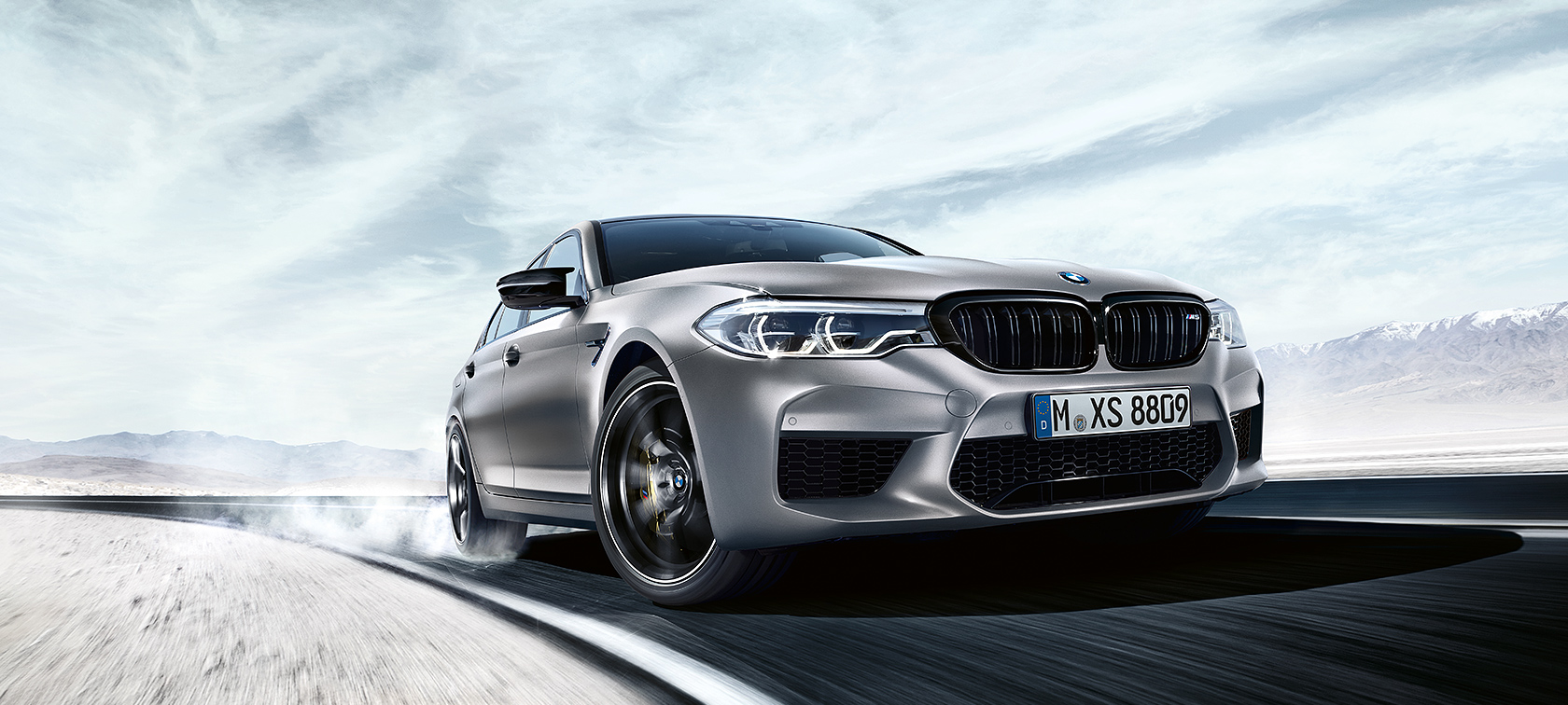 BMW M5 Competition in action Grey BMW M5 Competition driving on highway in front of snowy landscape