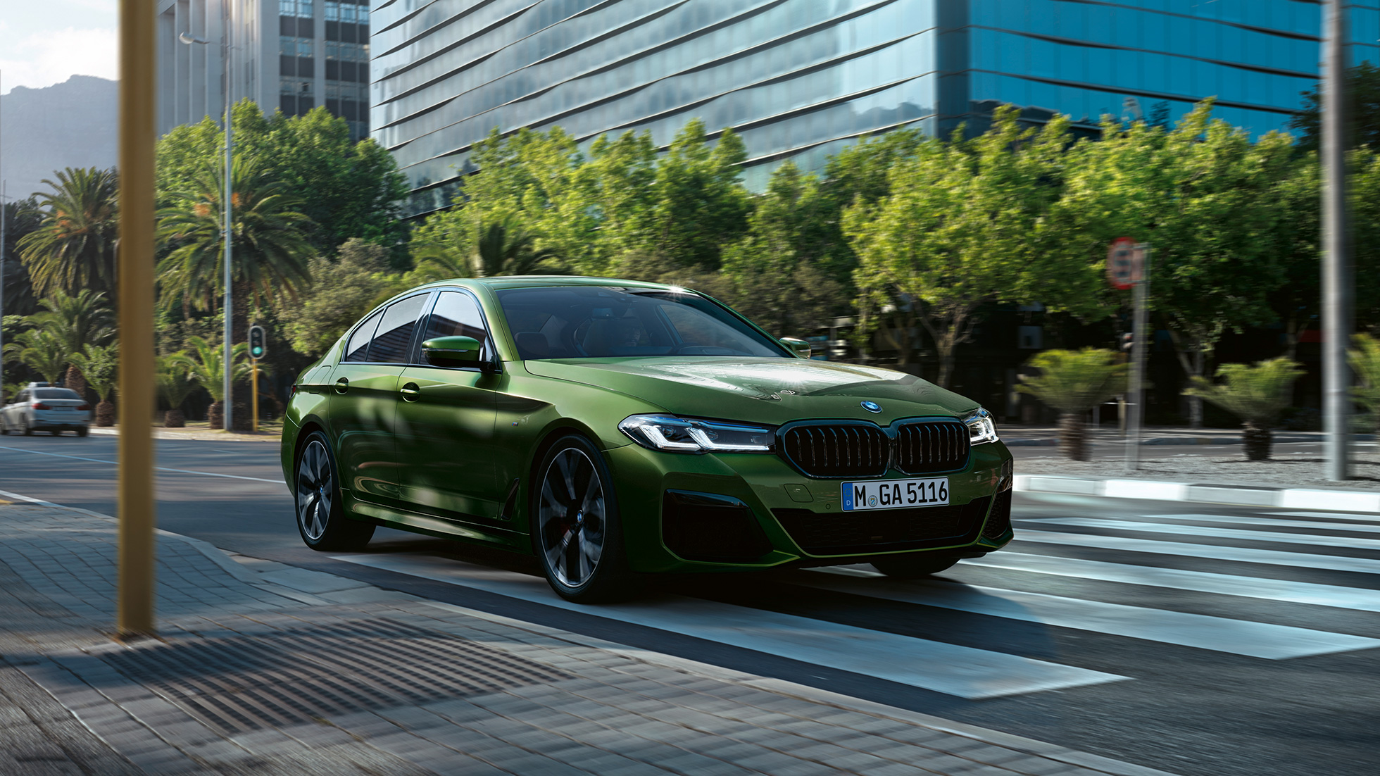 BMW M550i xDrive Sedán G30 LCI Renovación 2020 Vista de tres cuartos del frontal en marcha BMW M550i xDrive Sedán G30 LCI Renovación 2020 BMW Individual Verde Ermes metalizado Vista de tres cuartos del frontal en marcha en la ciudad