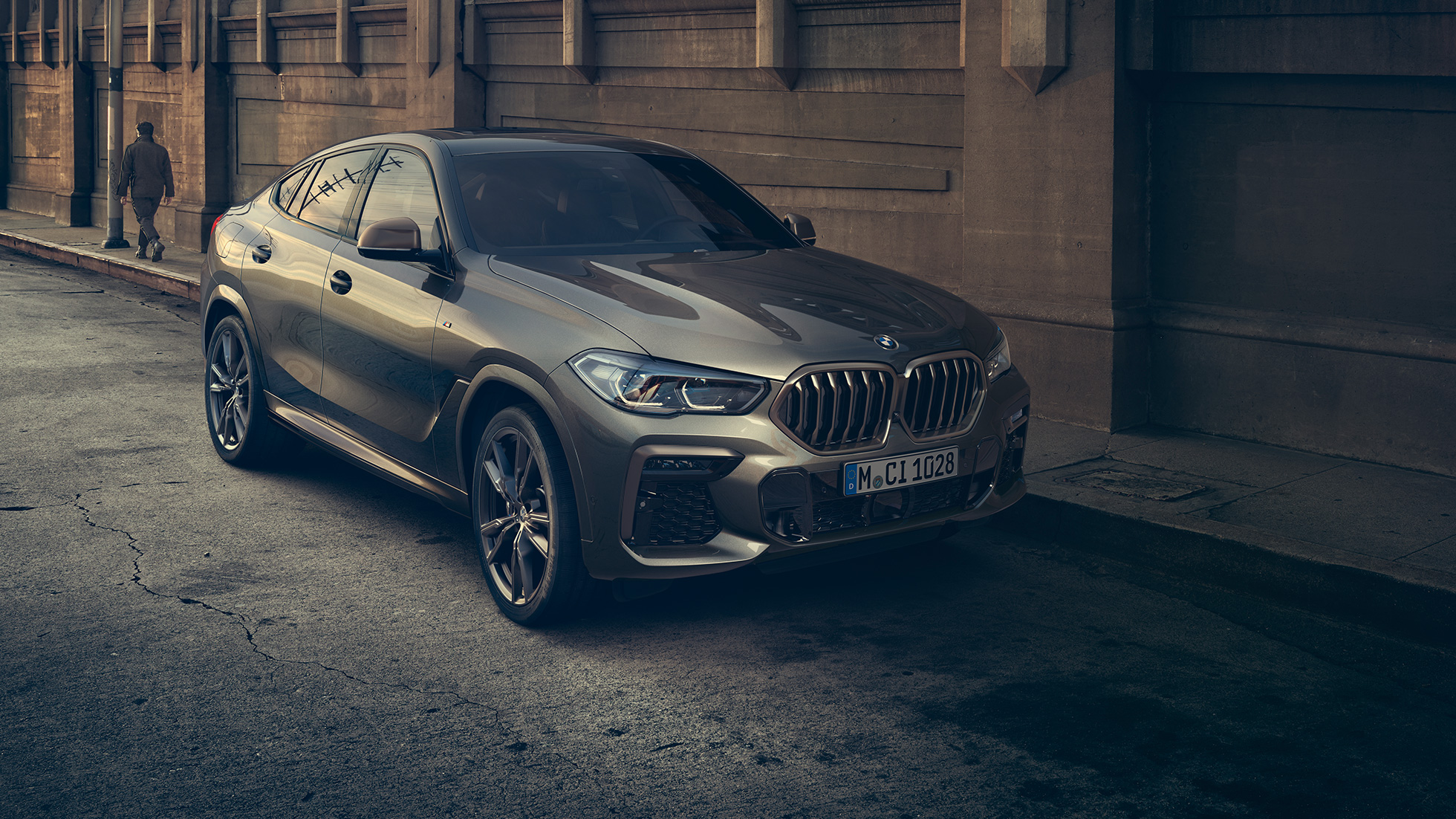 BMW X6 M50i parado. BMW X6 M50i en perspectiva frontal de tres cuartos parado frente a un escenario urbano.