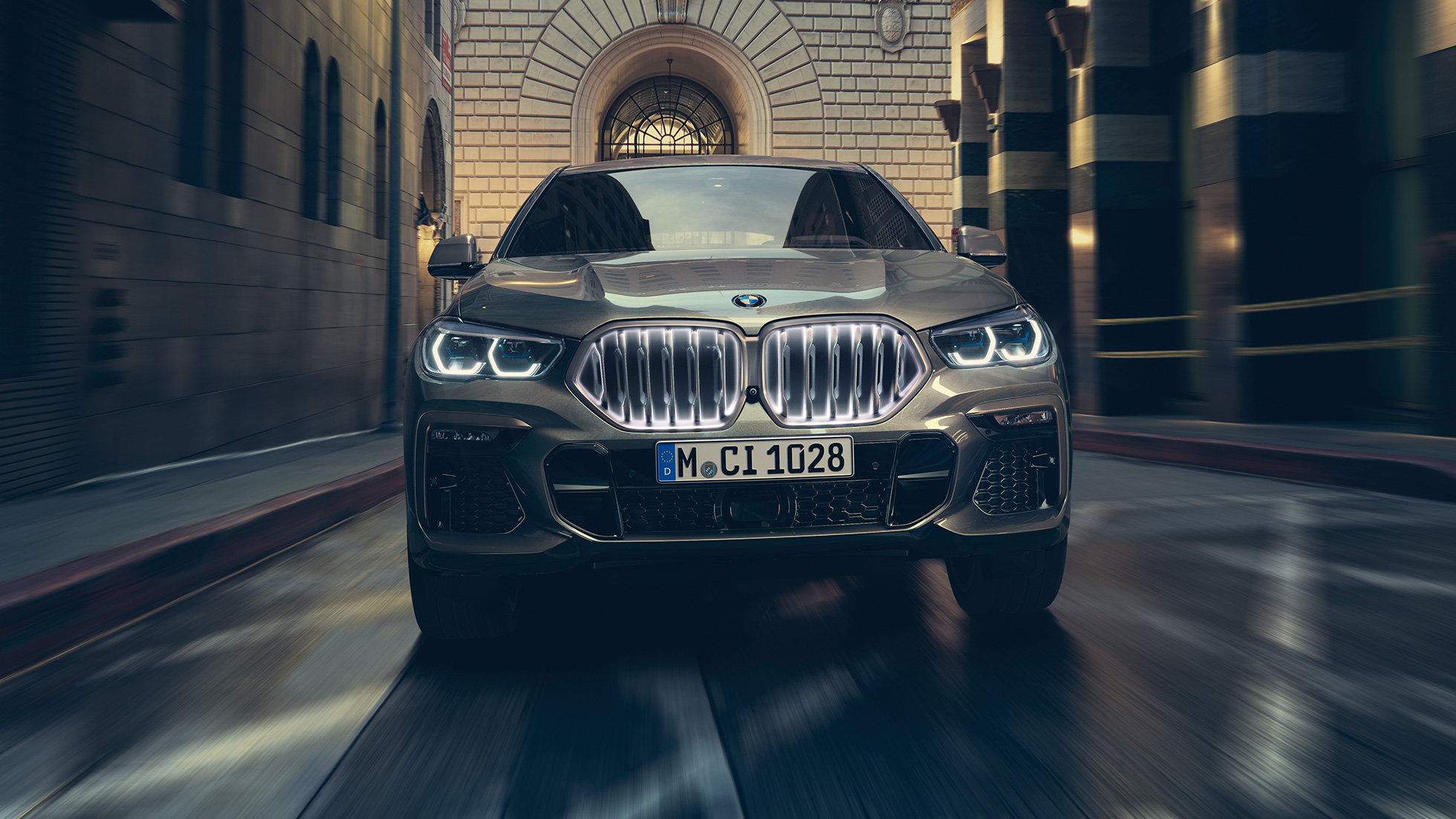BMW X6 M50i con parrilla de riñón BMW, ‘Iconic Glow’. BMW X6 M50i en perspectiva frontal enfrente de un escenario urbano.