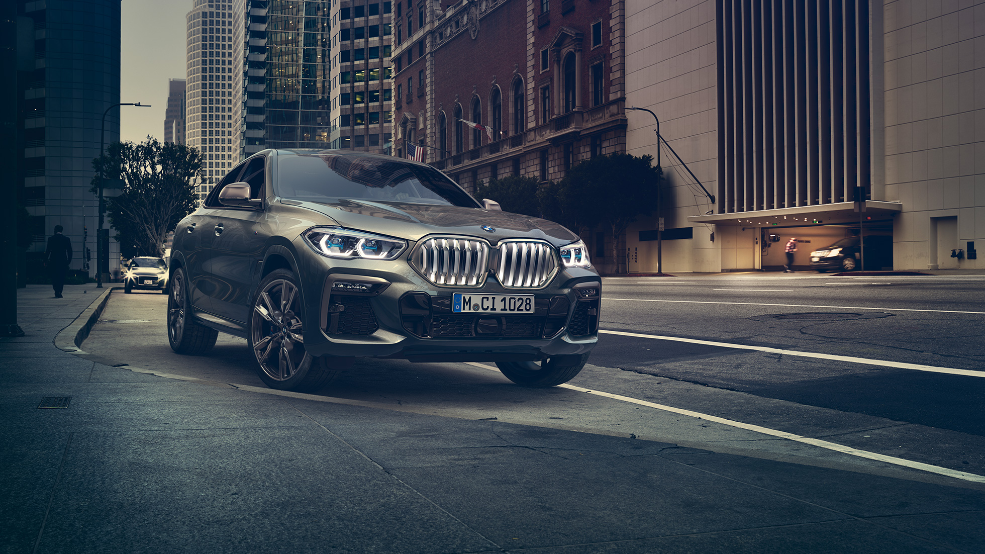 BMW X6 M50i detenido. BMW X6 M50i en perspectiva frontal de tres cuartos parado frente a un escenario urbano.