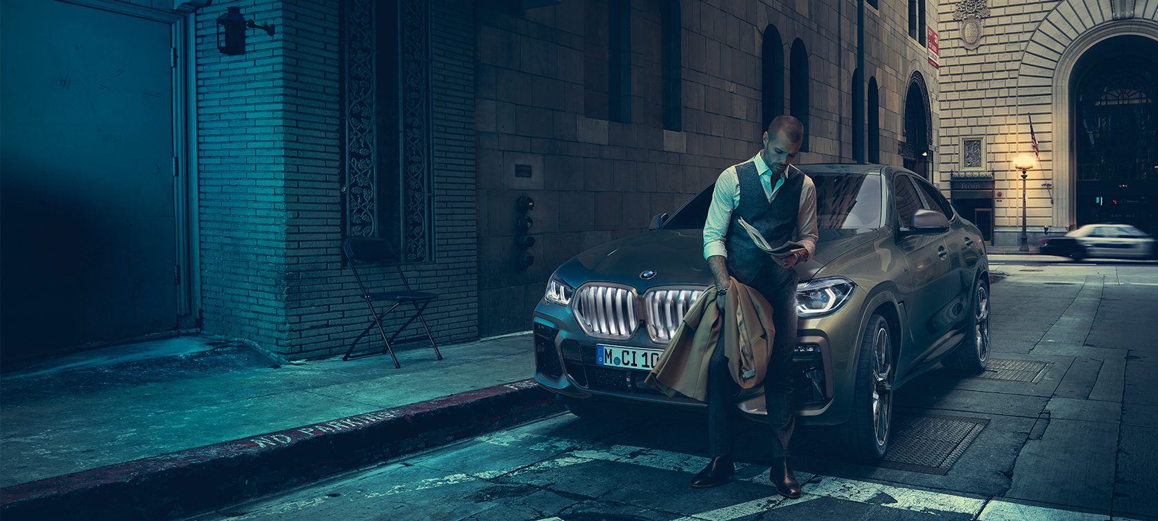Parte frontal del BMW X6 M50i. Hombre apoyado enfrente del BMW X6 M50i.