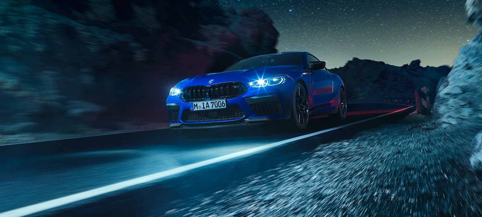 BMW M8 Competition Coupé, vista frontal tres cuartos. El BMW M8 Competition Coupé en Marina Bay Blue metálico, vista frontal tres cuartos, conduciendo de noche.