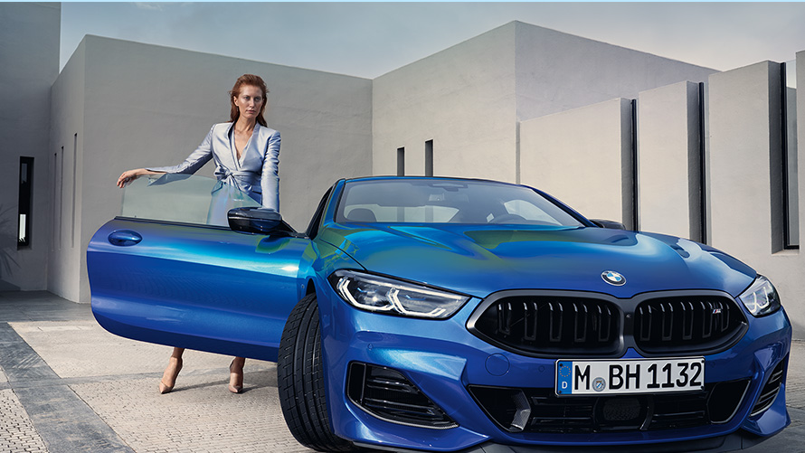Nuevo BMW M850i xDrive Coupé G15 LCI Renovación 2022 M Portimao Blue metalizado, vista del frontal, parado, con modelo femenina en la puerta abierta del acompañante