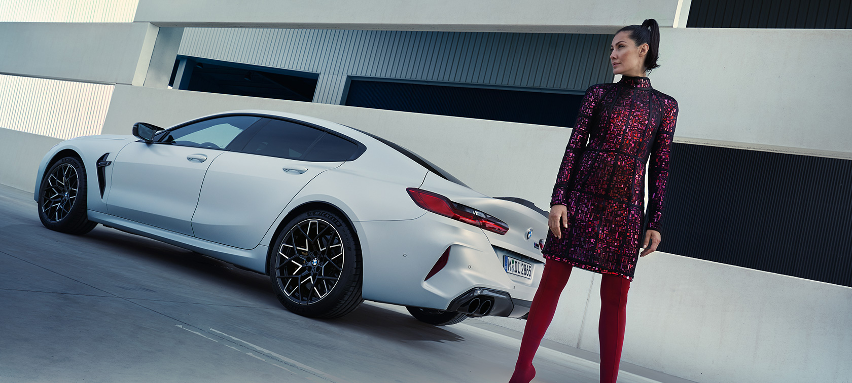 Vista de tres cuartos de la zaga nuevo BMW M8 Competition Gran Coupé F93 LCI 2022 Nuevo BMW M8 Competition Gran Coupé F93 LCI Renovación 2022 BMW Individual Frozen Brilliant White metalizado, vista de tres cuartos de la zaga, con modelo femenina junto a un vehículo