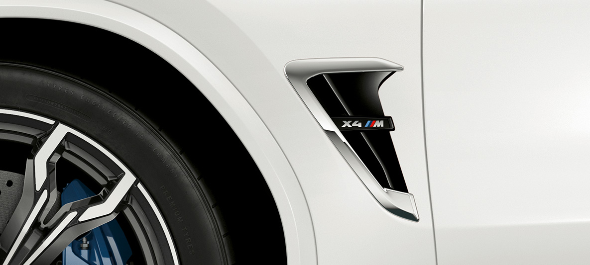 BMW X4 M, aleta M. BMW X4 M en Alpine White, exterior, aleta M con partes cromadas y designación de modelo.