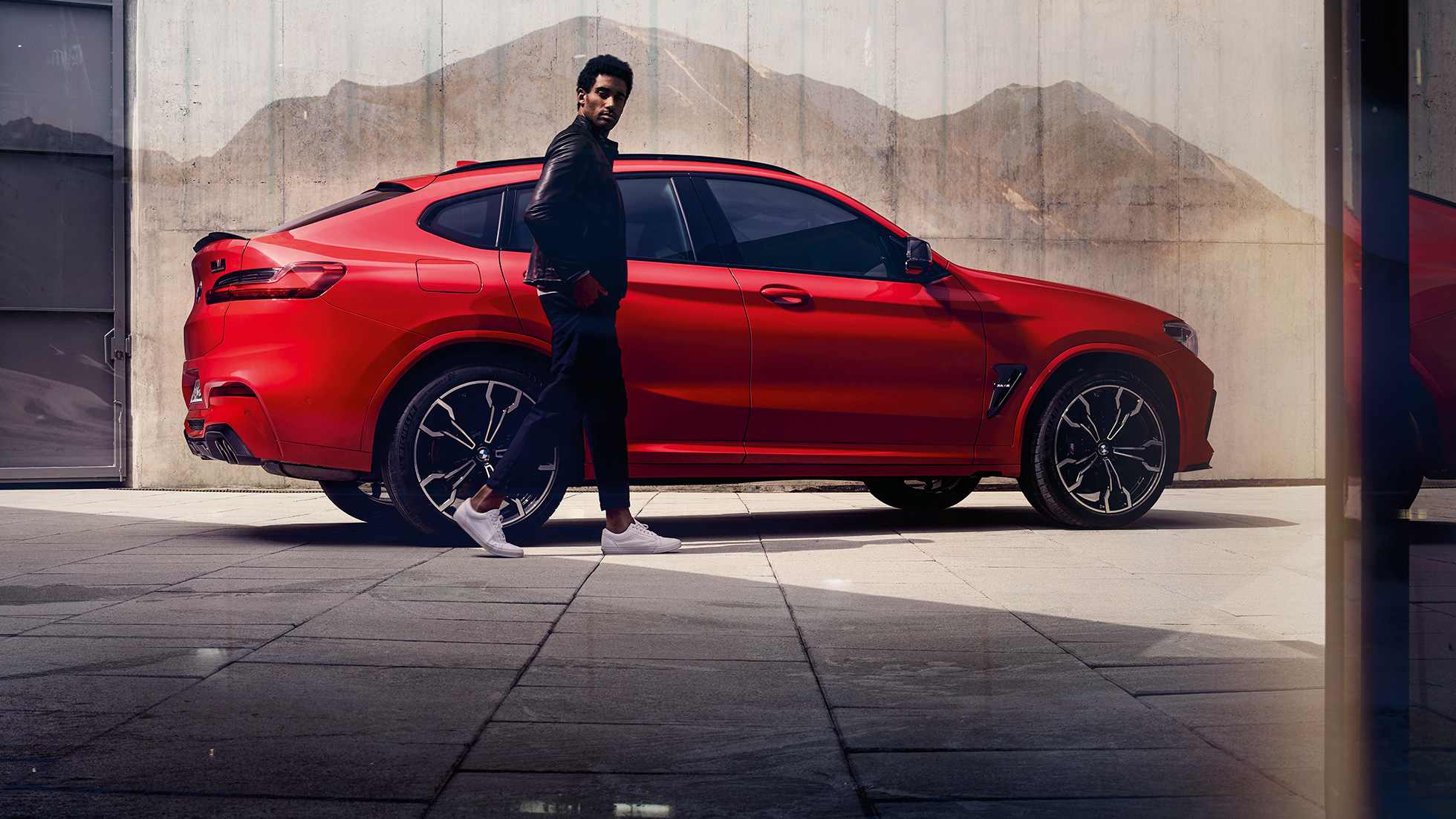 BMW X4 M Competition, vista lateral con hombre joven. BMW X4 M Competition en Toronto Red metálico, exterior, vista lateral con hombre joven.