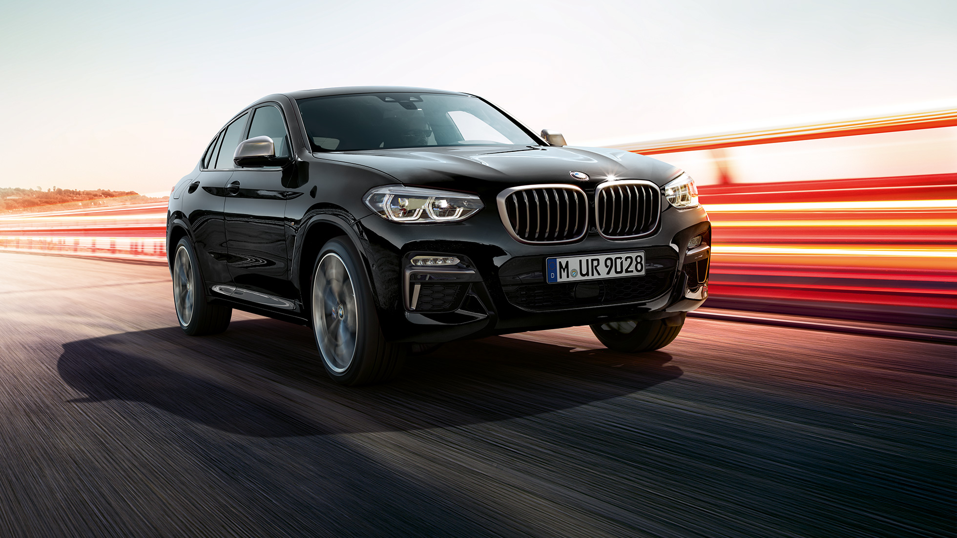 BMW X4 M40i, vista delantera de tres cuartos. BMW X4 M40i en Black Sapphire metálico, exterior, vista delantera de tres cuartos, lado izquierdo con franjas claras.