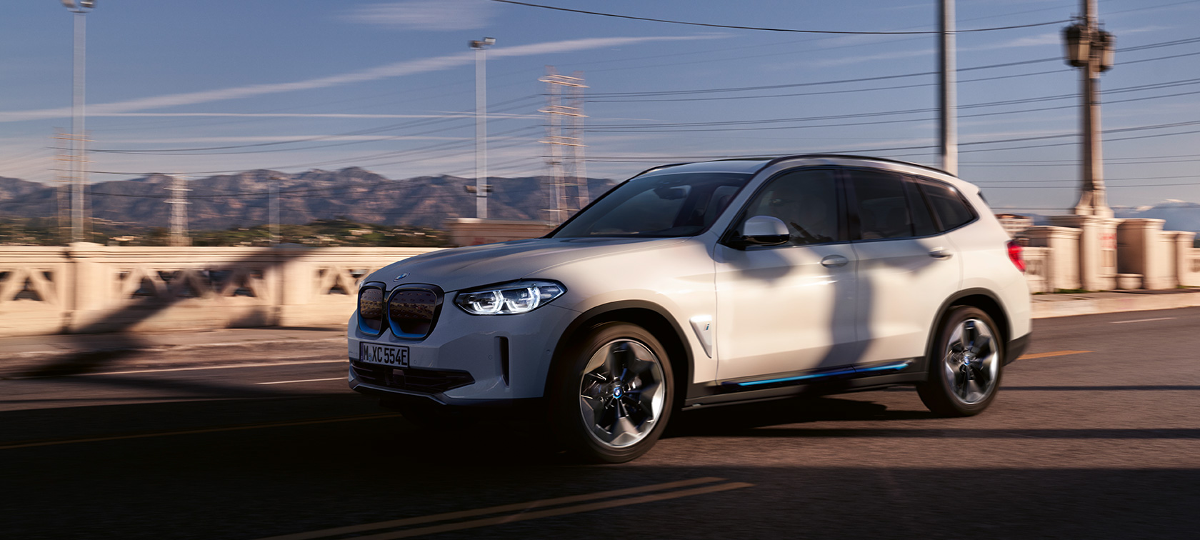 BMW iX3 G08 Vista de tres cuartos del frontal, en marcha en la carretera BMW iX3 G08 2020 Mineralweiss metalizado Vista de tres cuartos del frontal, en marcha en carretera