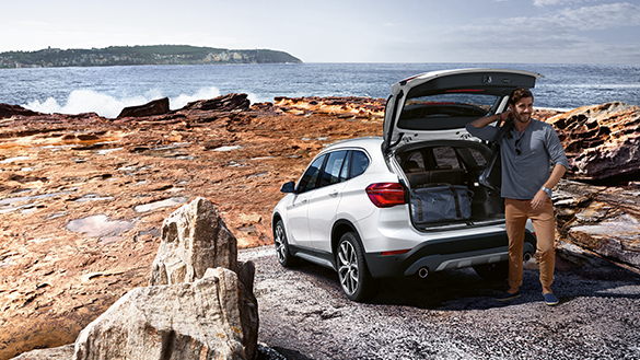 BMW X1 blanco con cajuela abierta y mar al fondo BMW X1 blanco con cajuela abierta y mar al fondo