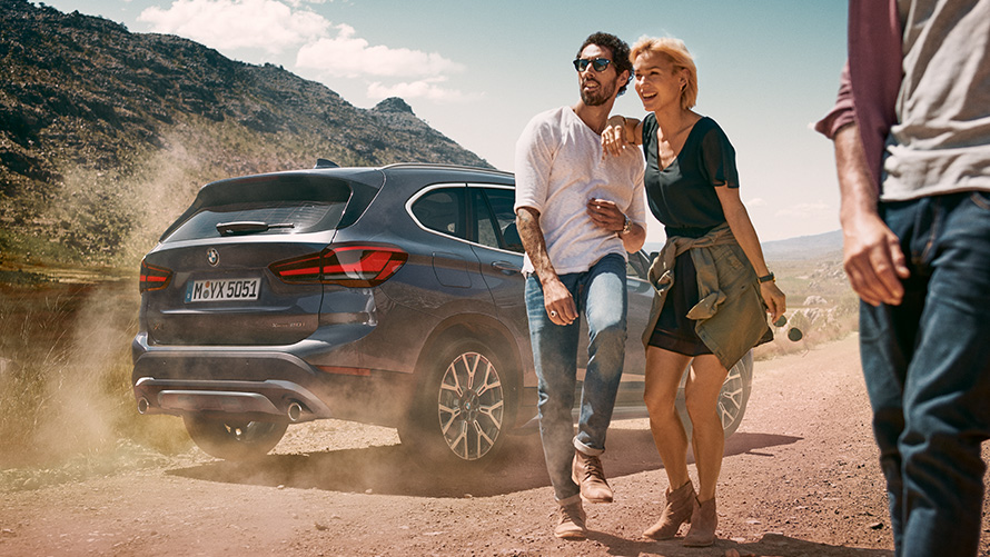 BMW X1 F48 LCI Storm Bay, vista de tres cuartos de la zaga BMW X1 F48 LCI Storm Bay, vista de tres cuartos de la zaga, parado, en un paisaje con personas delante