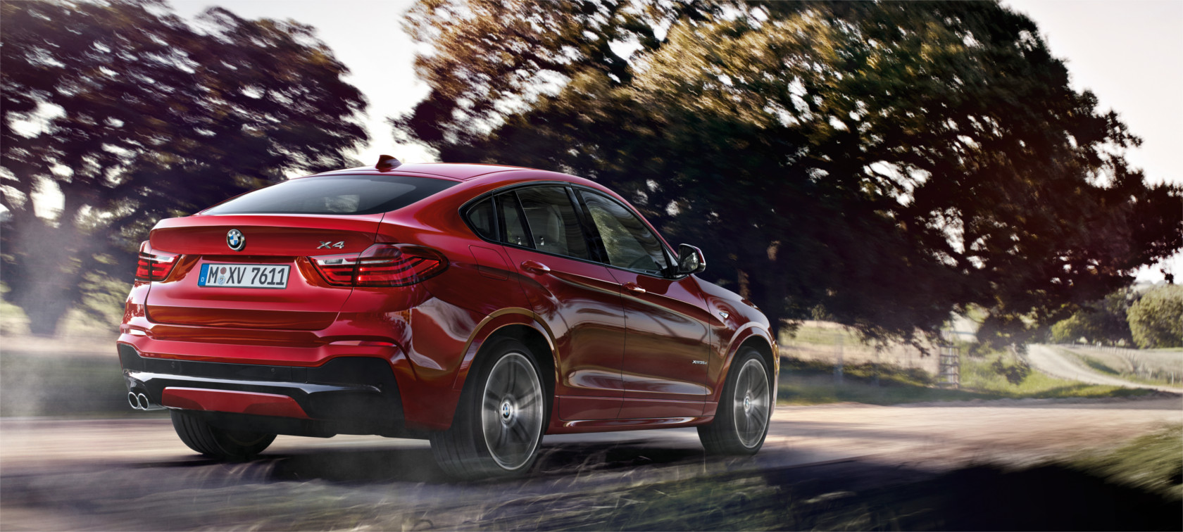 Nuevo BMW X4 rojo avanzando por las carretera con árboles al fondo Nuevo BMW X4 rojo avanzando por las carretera con árboles al fondo