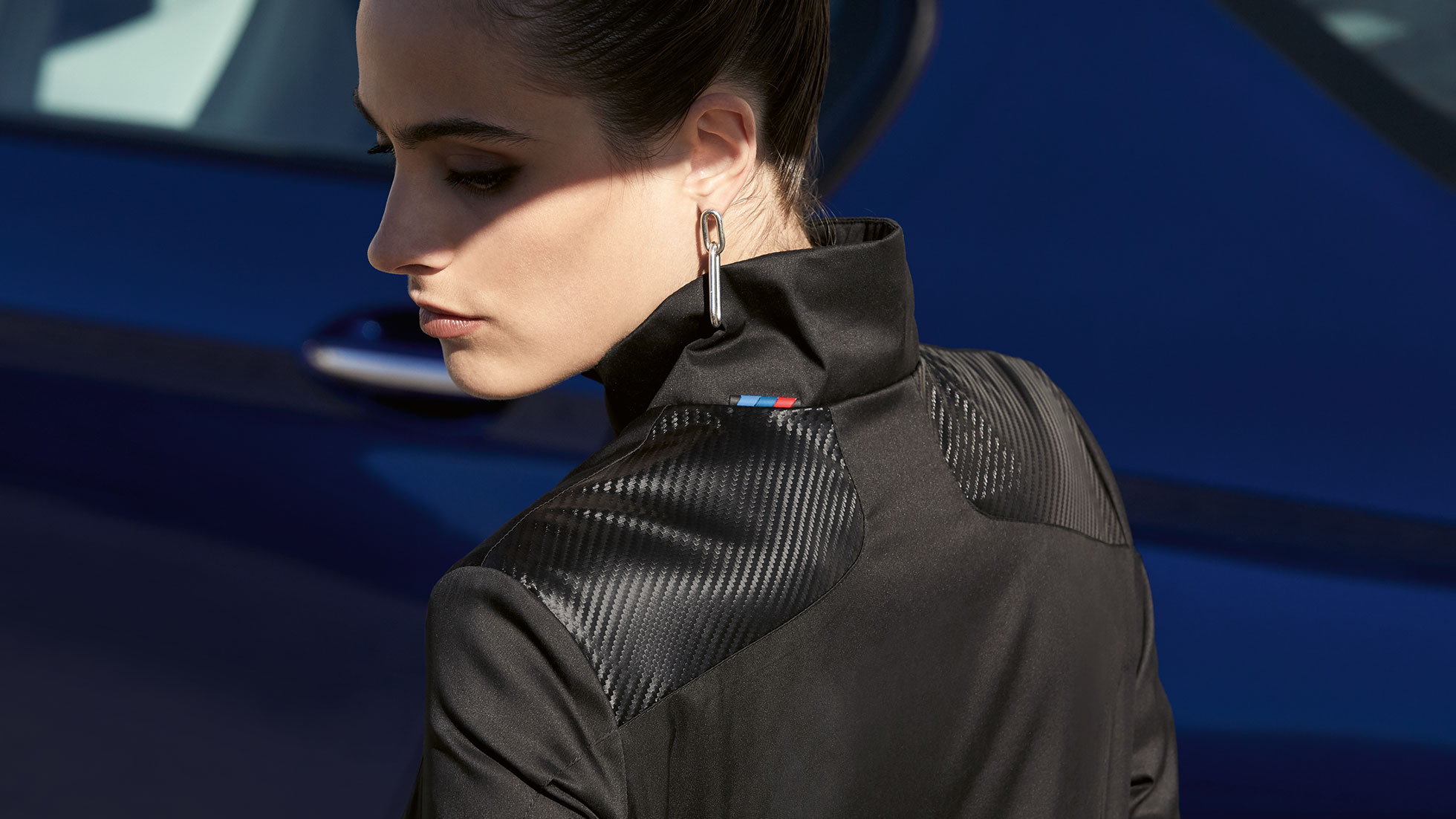 Chamarra BMW M, para mujer. Se muestra a una mujer con una chamarra BMW M, para mujer de la colección BMW M. Detalle de la mezcla de materiales.