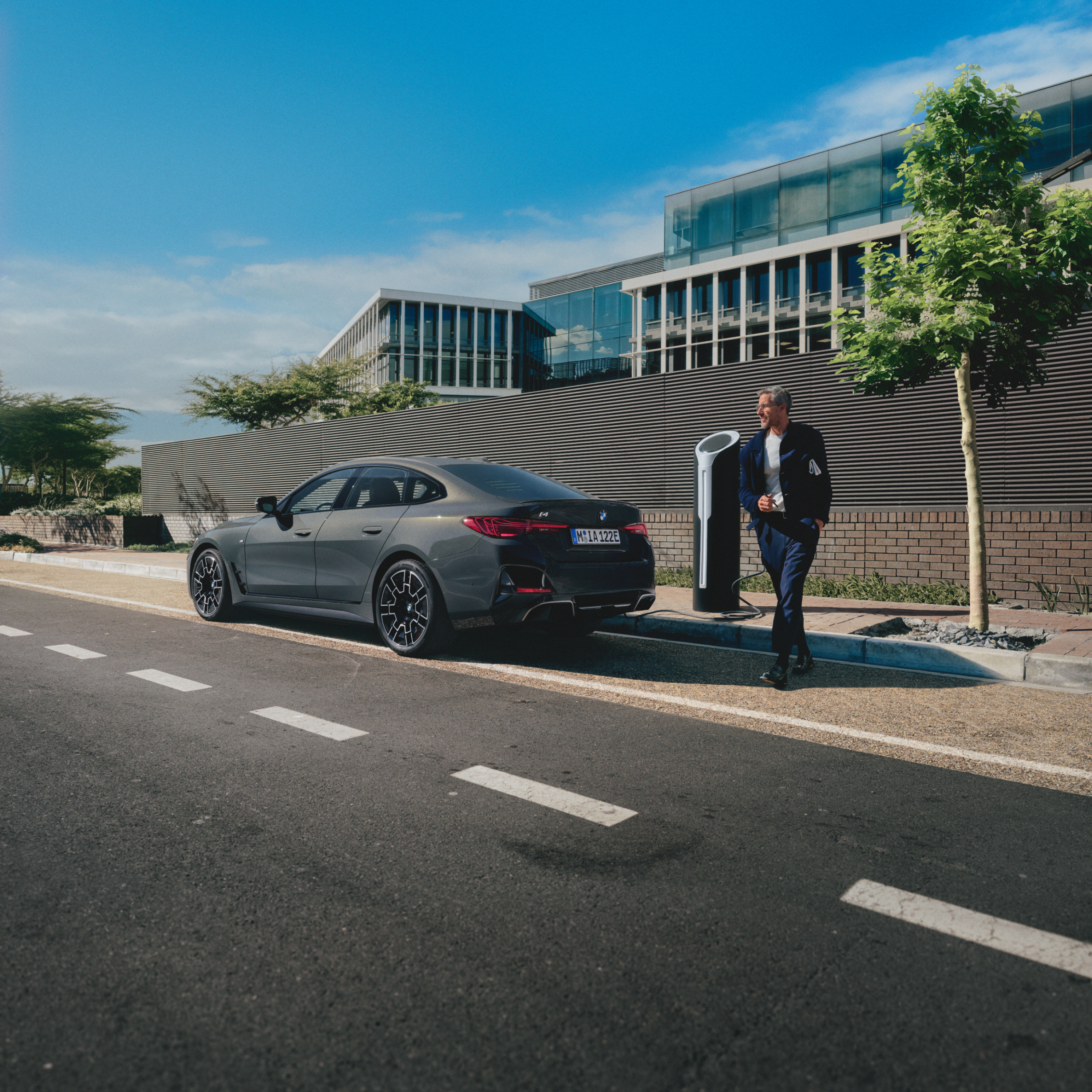 Persona de pie detrás de un BMW cargándose a un lado de la carretera